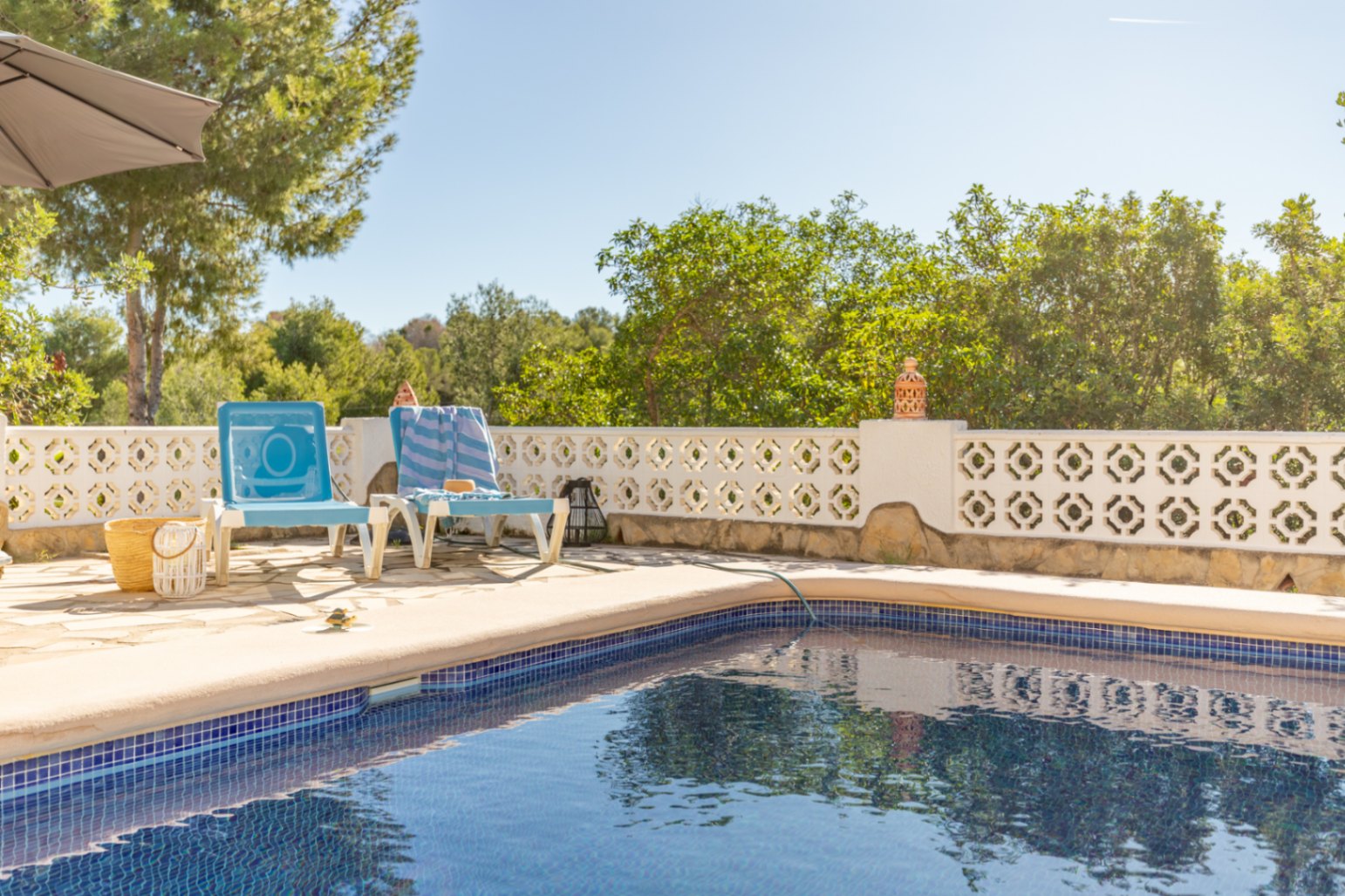 Piscina con gresite azul y terraza de piedra natural, rodeada por un muro de celosía blanca y vegetación mediterránea madura que garantiza privacidad.