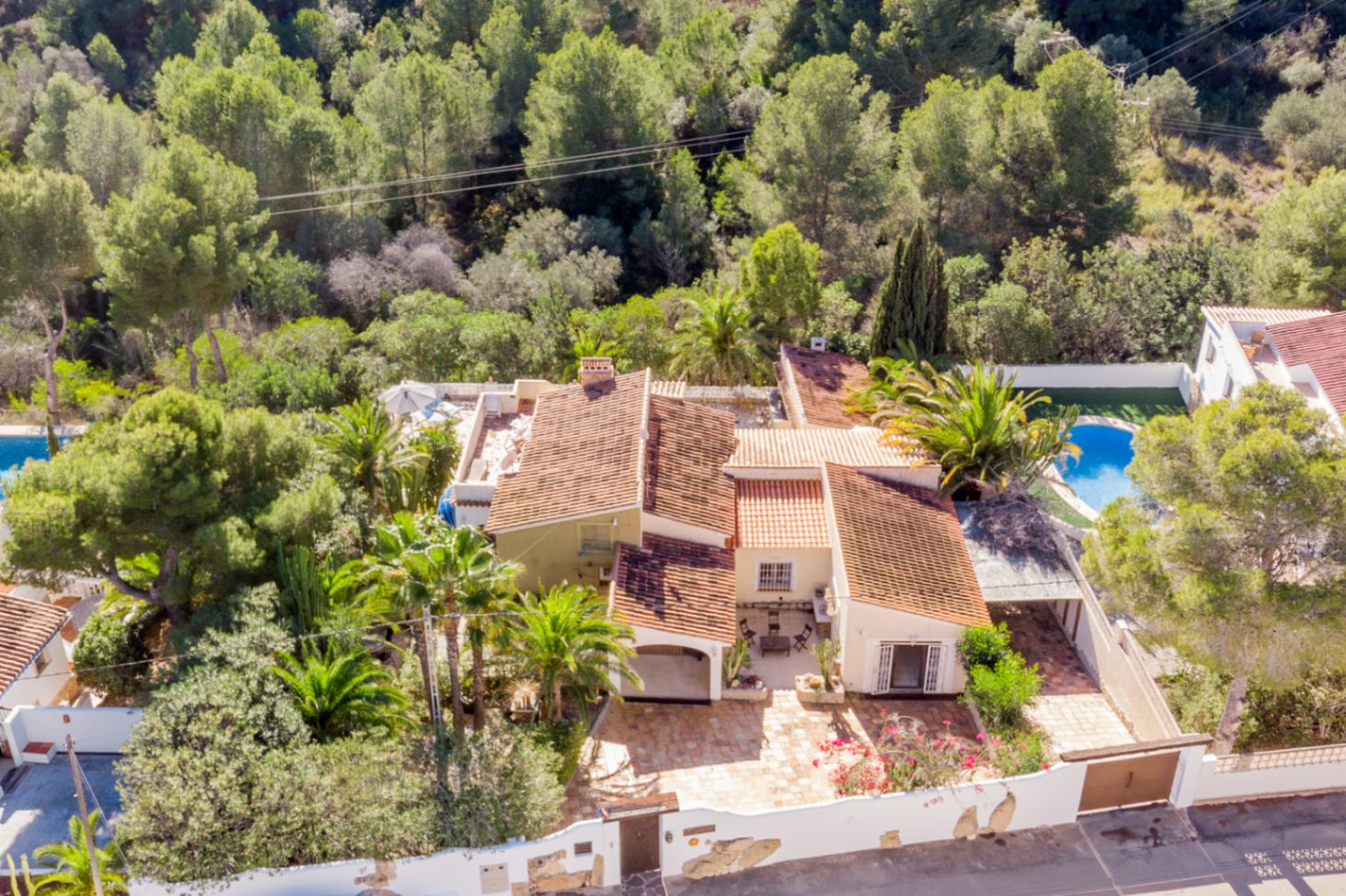 Vista aérea de la villa destacando su arquitectura mediterránea con tejados de teja, rodeada de una zona verde protegida y palmeras maduras que garantizan privacidad.