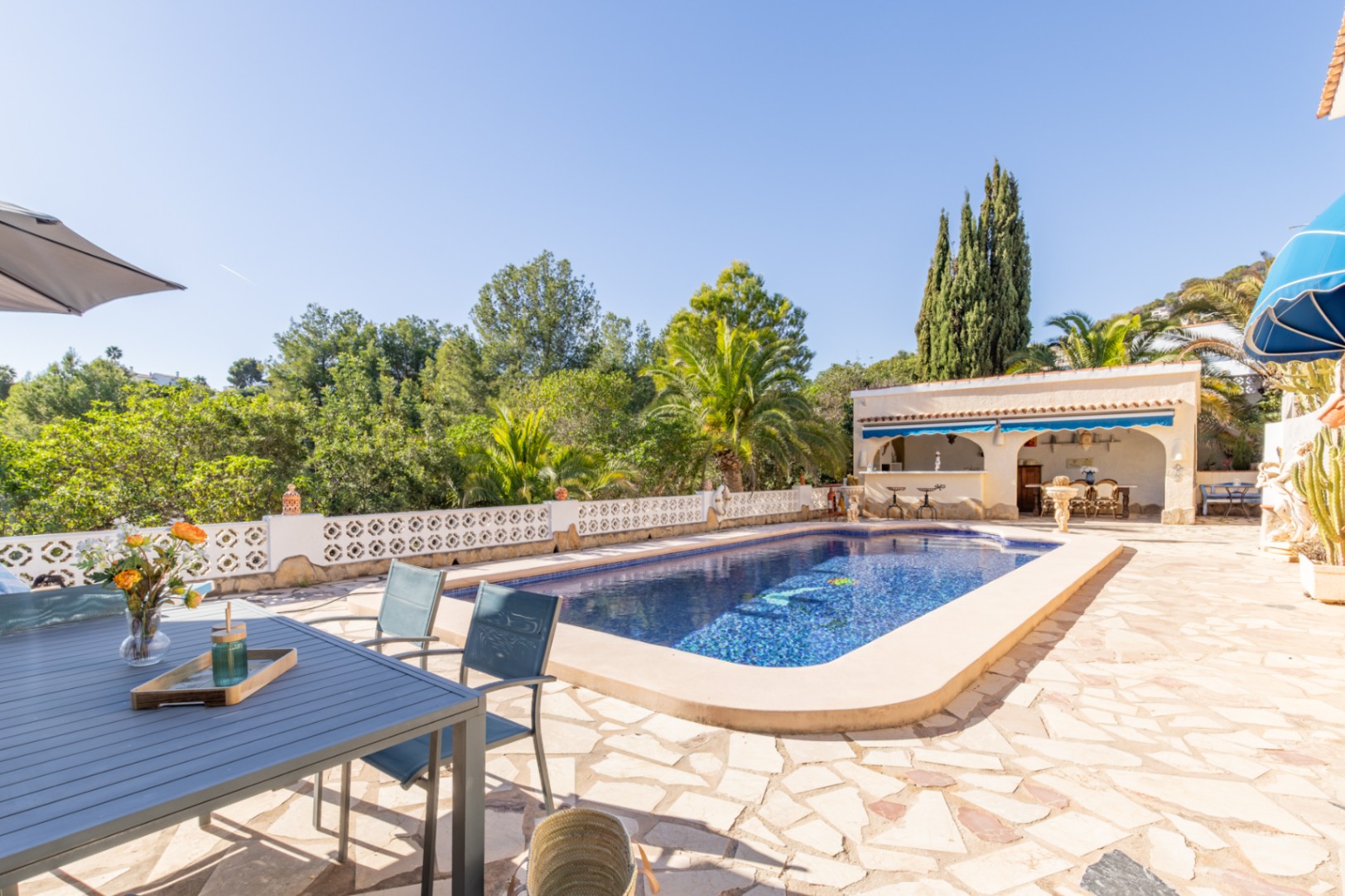 Zona exterior con piscina de 42 m², terraza de piedra natural y cocina de verano techada, rodeada de vegetación madura y vistas a la zona verde.