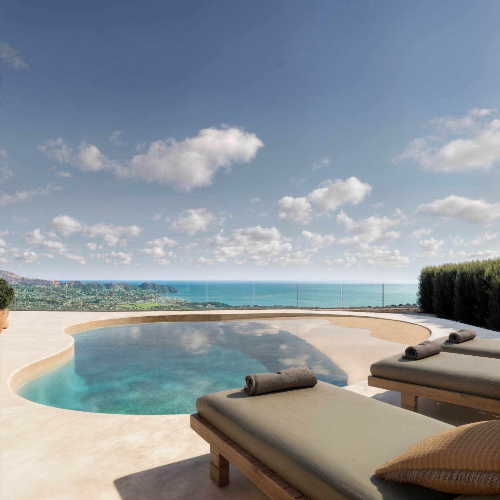 Terraza exterior con piscina de forma orgánica y zona de playa, tumbonas de madera y vistas panorámicas al mar Mediterráneo protegidas por barandilla de cristal.