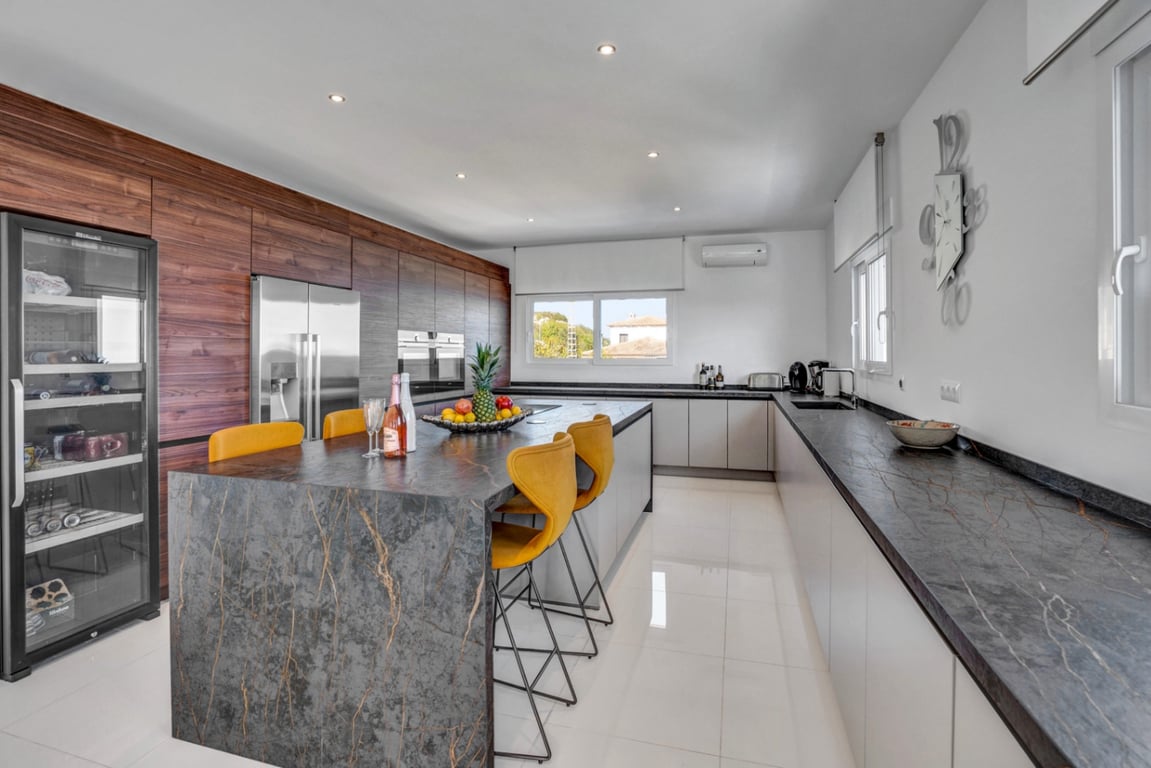 Cocina de diseño con isla central de piedra oscura, taburetes amarillos, electrodomésticos integrados, vinoteca y armarios de madera natural.