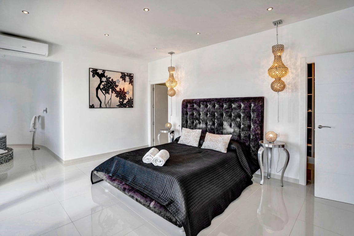 Dormitorio con cabecero de terciopelo capitonné, suelos de gres porcelánico brillante, lámparas colgantes decorativas y sistema de aire acondicionado individual.