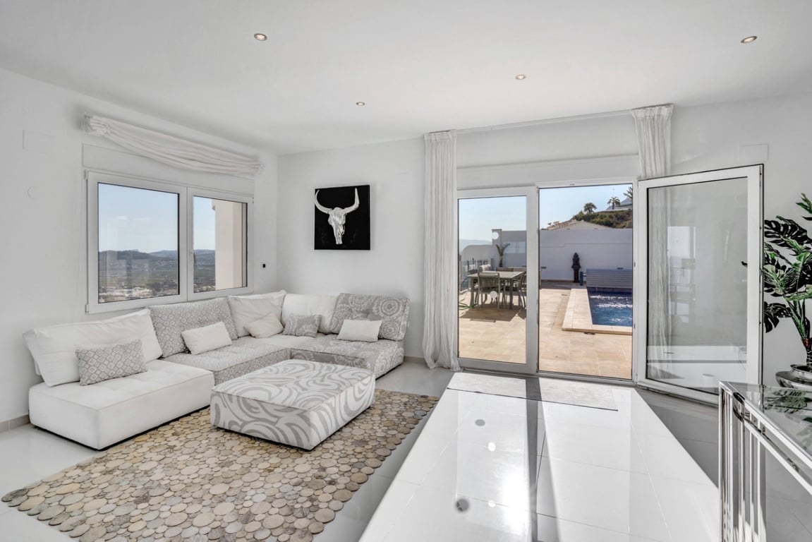 Salón luminoso con sofá modular y acceso directo a la terraza con piscina, ofreciendo vistas despejadas al mar y las montañas de Jávea.