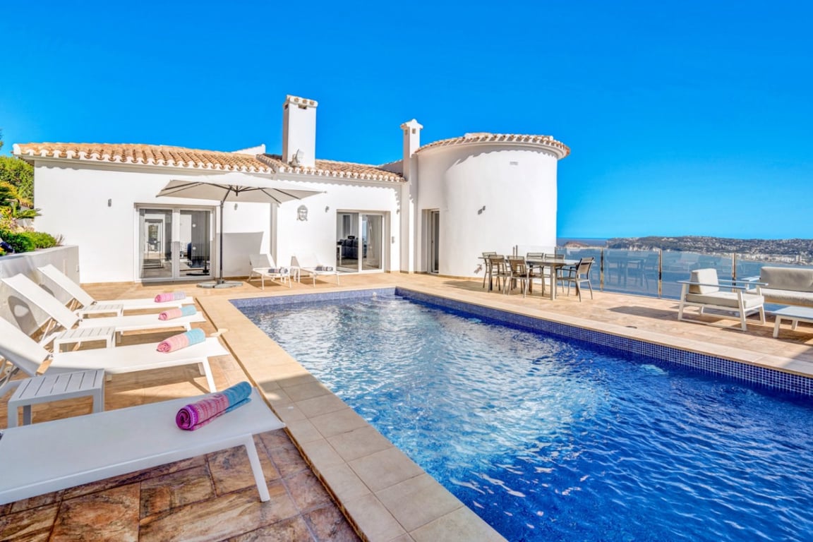 Terraza principal con piscina exterior, zona de solárium con hamacas y comedor al aire libre frente a las vistas panorámicas del puerto de Jávea.