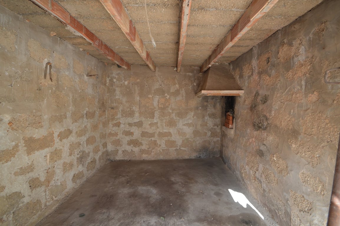Espacio diáfano con paredes de piedra vista, techos de vigas de madera y una chimenea rústica, ideal para reformar como estudio o zona de almacenamiento.