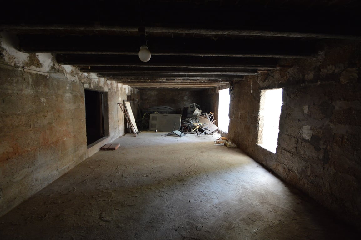Espacio diáfano con vigas de madera a la vista y muros de piedra original, ideal para convertir en un estudio o zona de almacenamiento con luz natural.