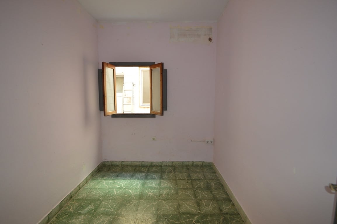 Habitación interior con suelos de baldosa verde veteada, paredes en tono malva suave y una ventana de madera que aporta luz natural desde el patio.