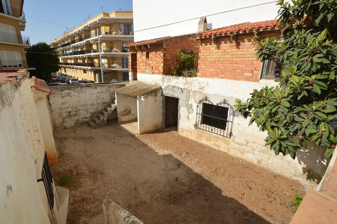 Patio privado con suelo de tierra y muros encalados, que incluye dependencias de ladrillo visto, escaleras exteriores y acceso trasero en el casco antiguo.