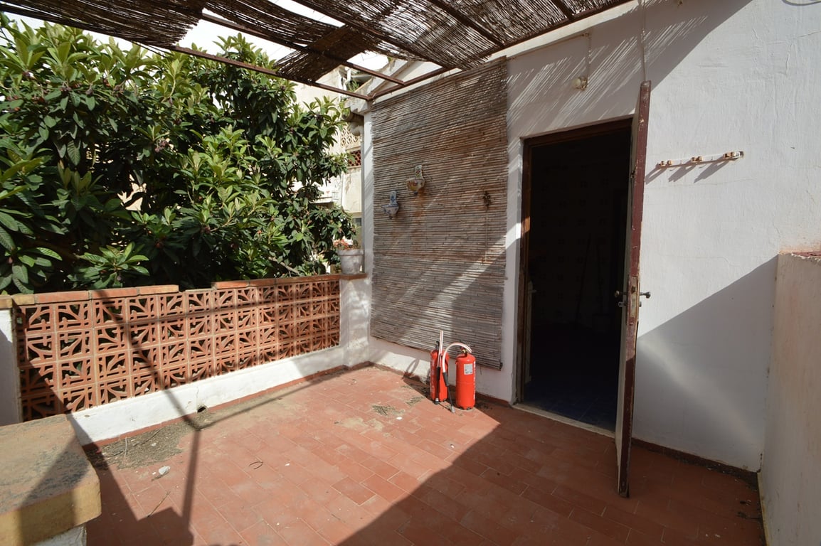Terraza exterior con suelo de baldosas de barro, pérgola de cañizo y muro perimetral de celosía cerámica junto a vegetación mediterránea.