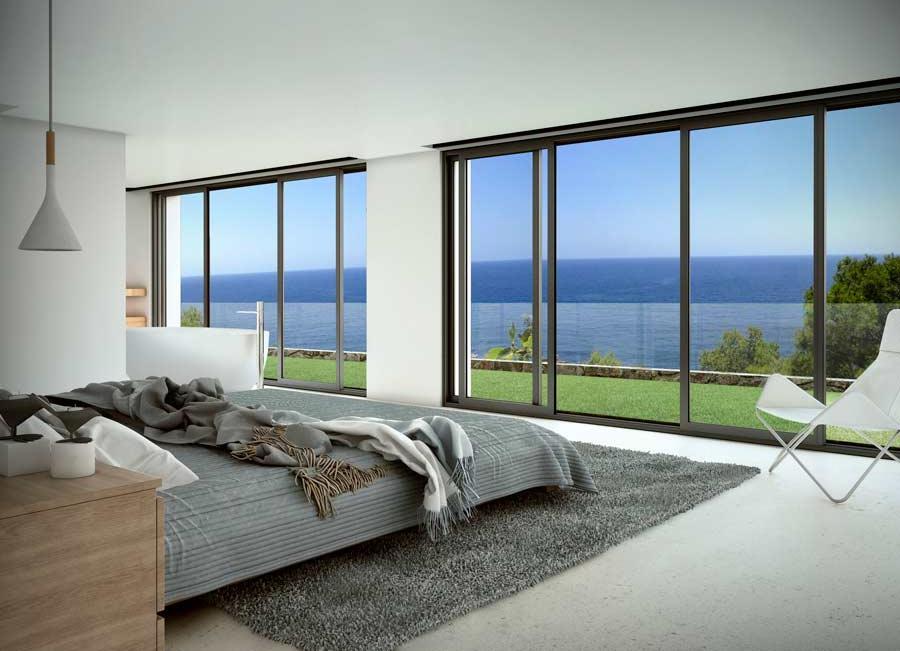 Dormitorio minimalista con ventanales de suelo a techo, cama con textiles grises y vistas panorámicas al mar Mediterráneo desde la zona de descanso y la bañera integrada.