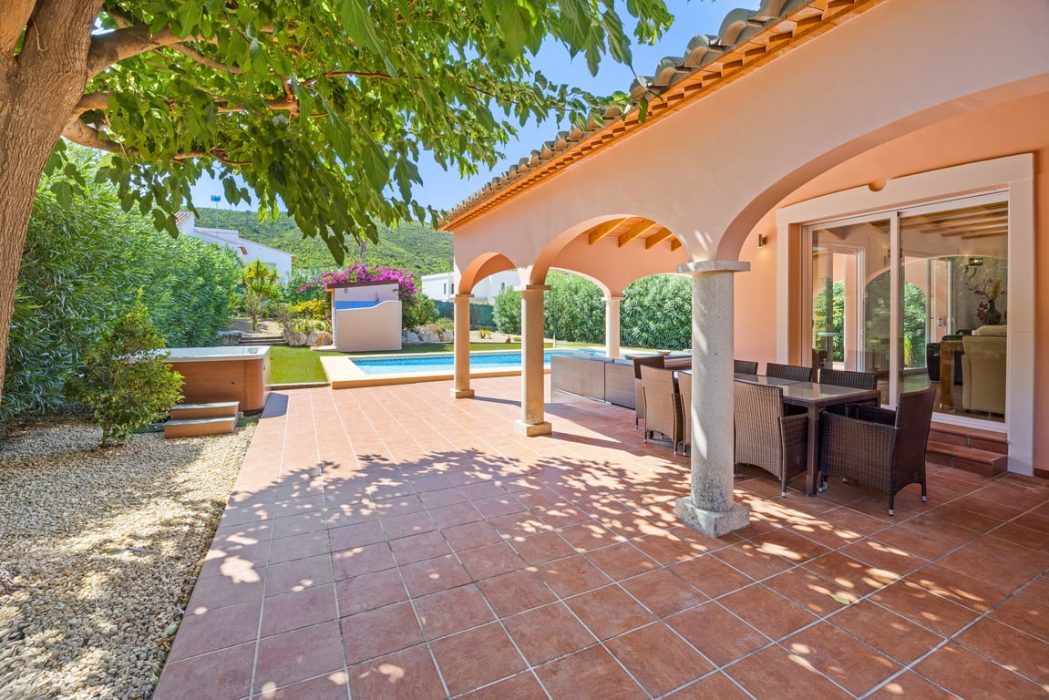 Amplia naya con arcos y columnas de piedra, equipada con comedor exterior sobre suelo de terracota, con vistas a la piscina, el jacuzzi y el entorno montañoso.