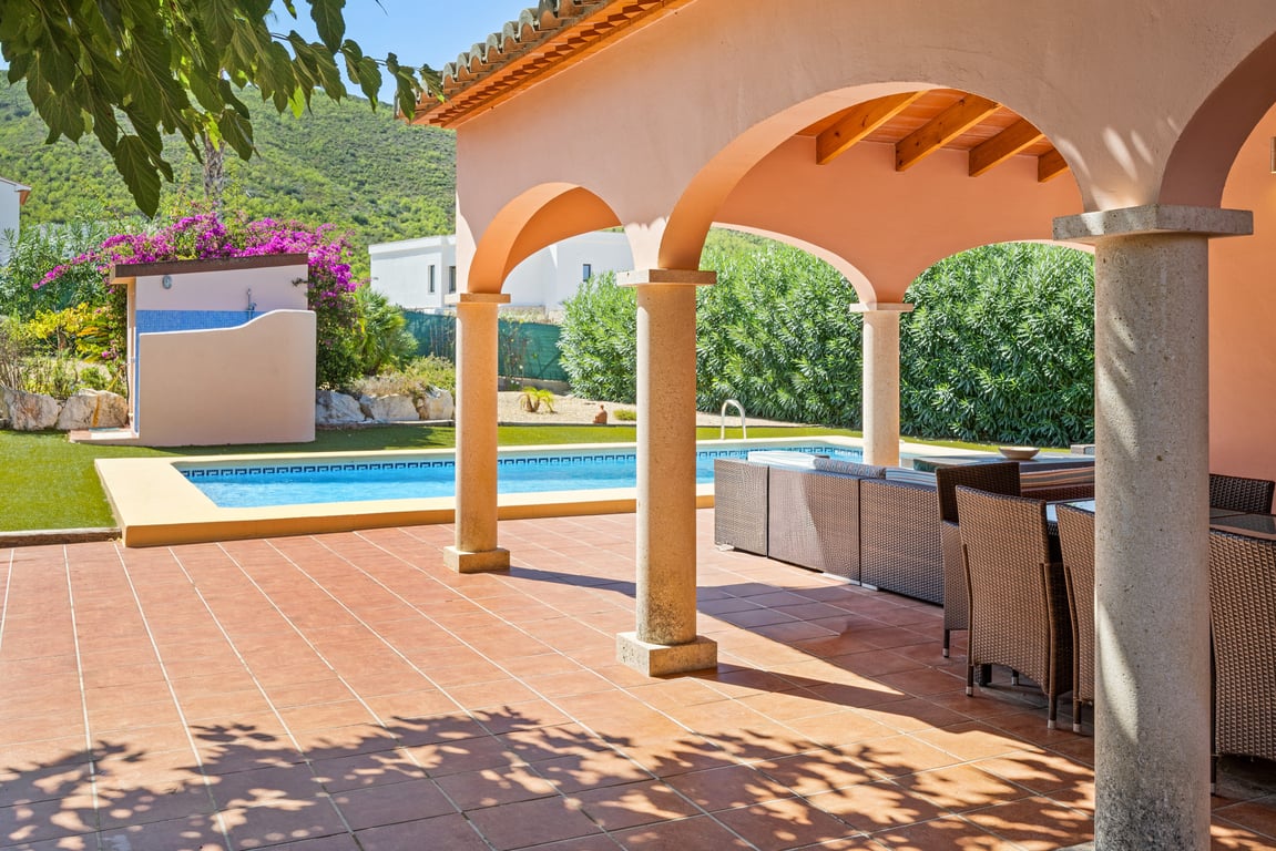 Amplia naya con arcos y columnas de piedra, vigas de madera a la vista y vistas directas a la piscina, zona de ducha exterior y las montañas.
