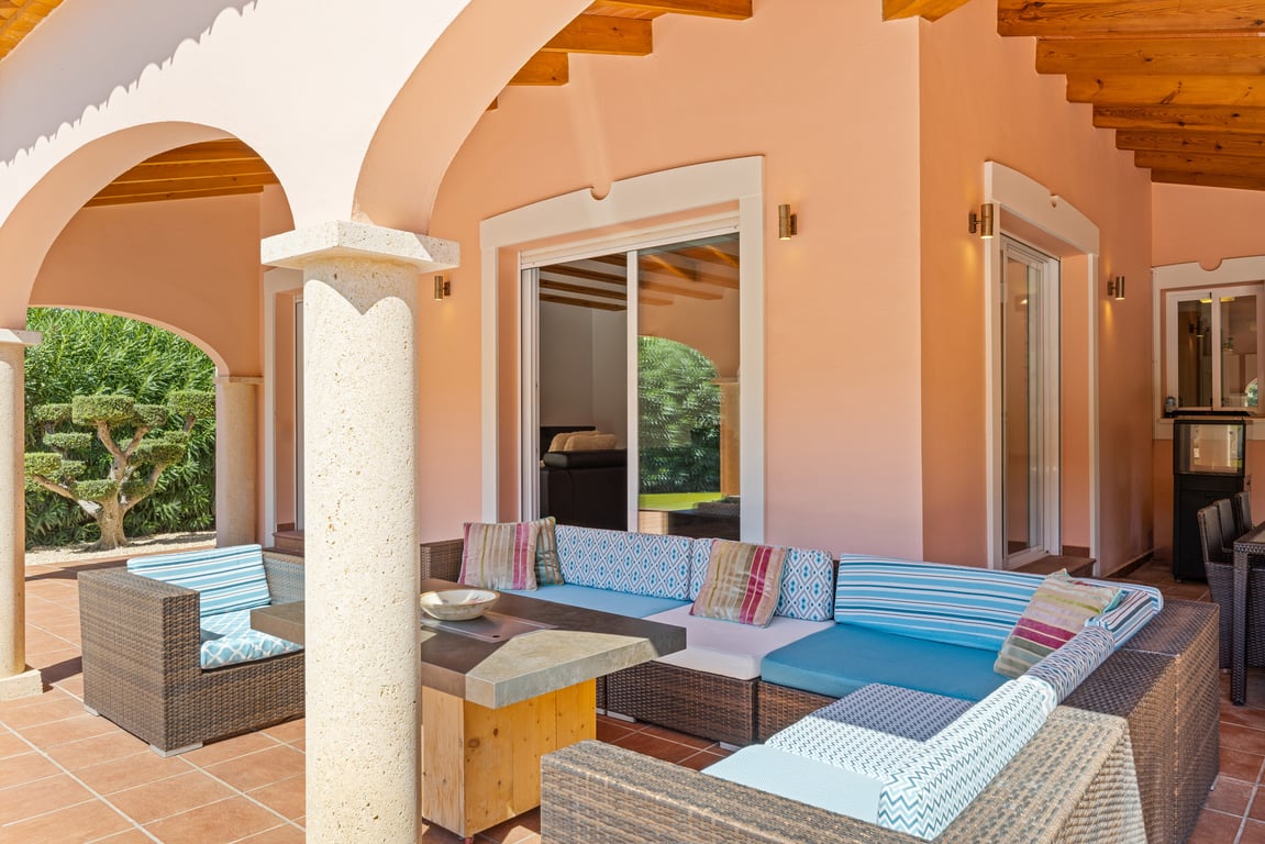Amplia naya cubierta con arcos tradicionales, columnas de piedra y vigas de madera. Incluye una zona de estar con sofás modulares y acceso directo al salón.