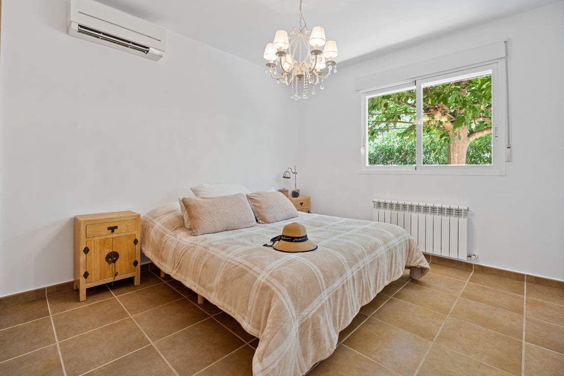 Dormitorio luminoso con suelos de gres, aire acondicionado split y calefacción central. Incluye una ventana con vistas al jardín y una lámpara de araña clásica.