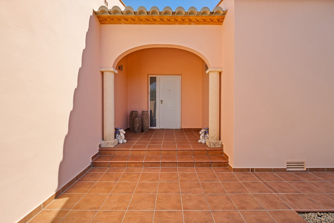 Entrada principal con porche arqueado, columnas de piedra Tosca y suelos de terracota. La fachada de tonos cálidos y los escalones de acceso definen el estilo mediterráneo de la villa.
