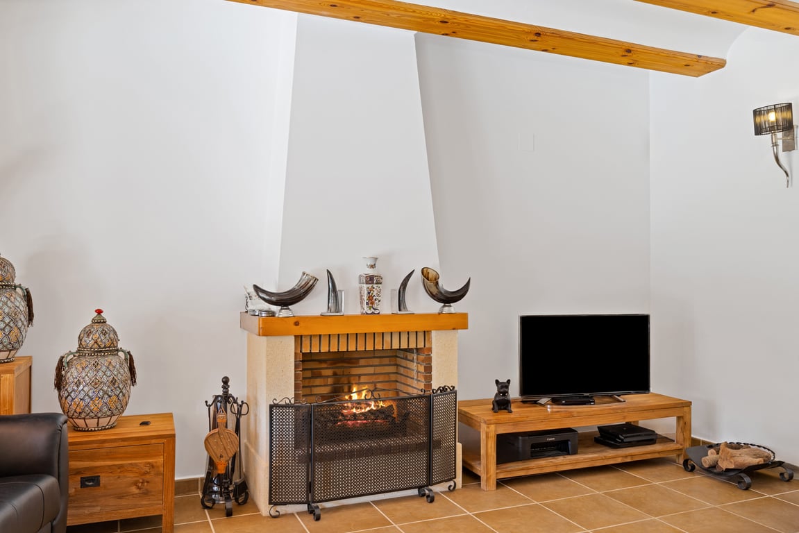 Salón con chimenea de obra, techos con vigas de madera vista y suelos cerámicos. Incluye mobiliario de madera y detalles decorativos tradicionales.