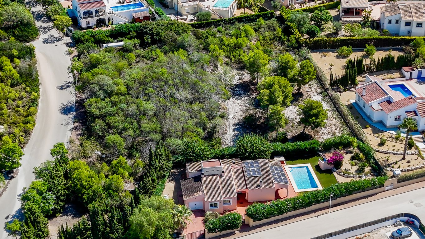 Vista aérea de la villa que muestra los paneles solares en el tejado, la piscina privada y el entorno arbolado en una parcela llana de Jávea.
