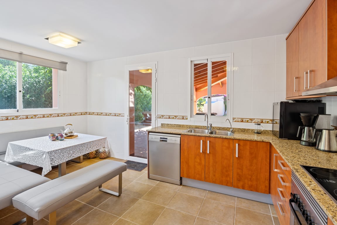 Cocina equipada en forma de L con encimera de granito, zona de desayuno con bancos tapizados y acceso directo al exterior a través de una puerta acristalada.