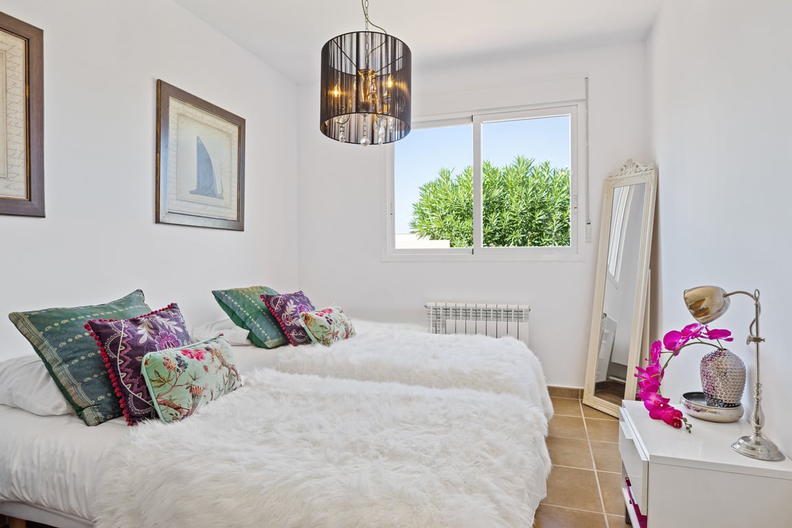 Dormitorio con dos camas individuales, colchas blancas de pelo largo, lámpara de techo negra con cristales y ventana con vistas a la vegetación.