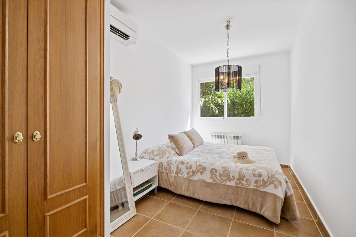 Dormitorio luminoso con suelos de gres, aire acondicionado split, armario empotrado de madera y ventana con vistas a la vegetación exterior.