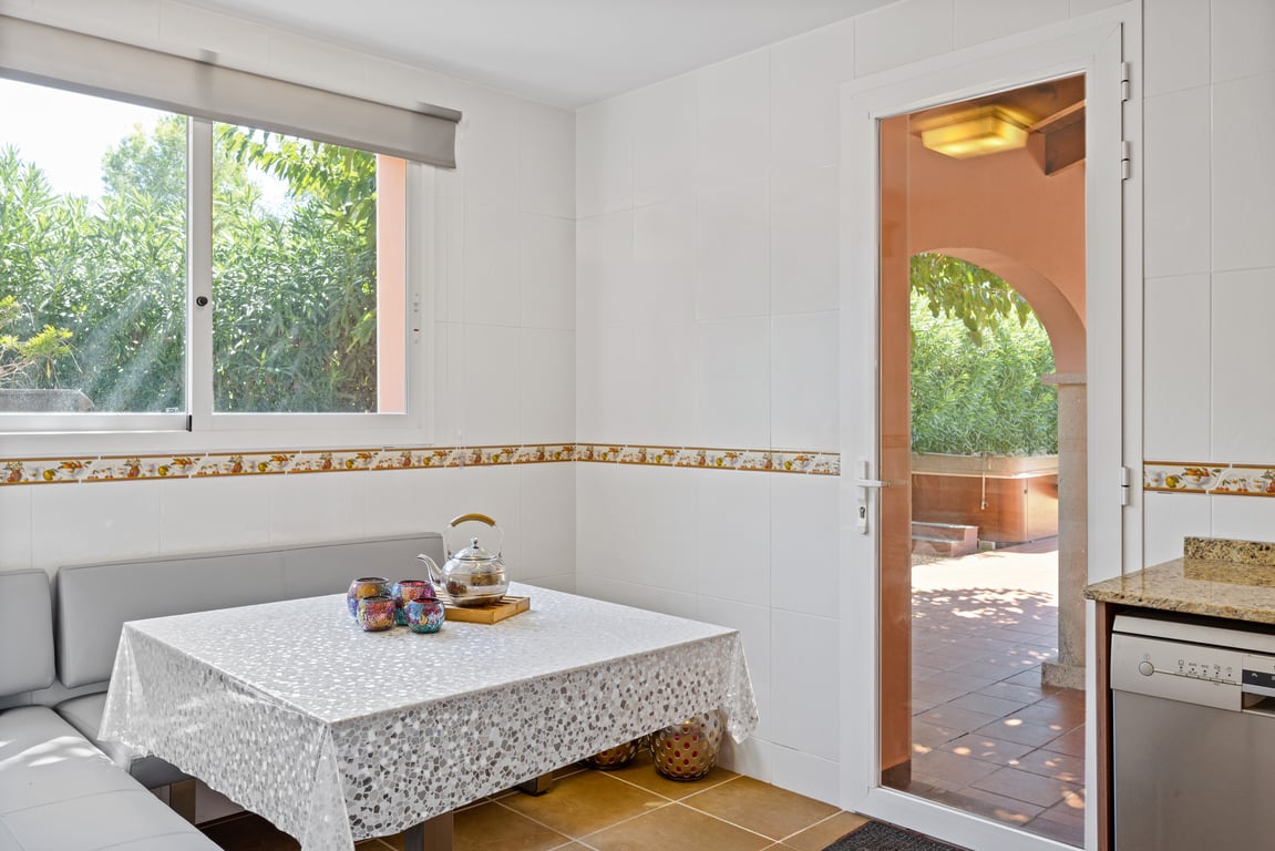 Rincón de desayuno en la cocina con banco esquinero, paredes alicatadas y puerta acristalada que comunica directamente con la naya exterior.