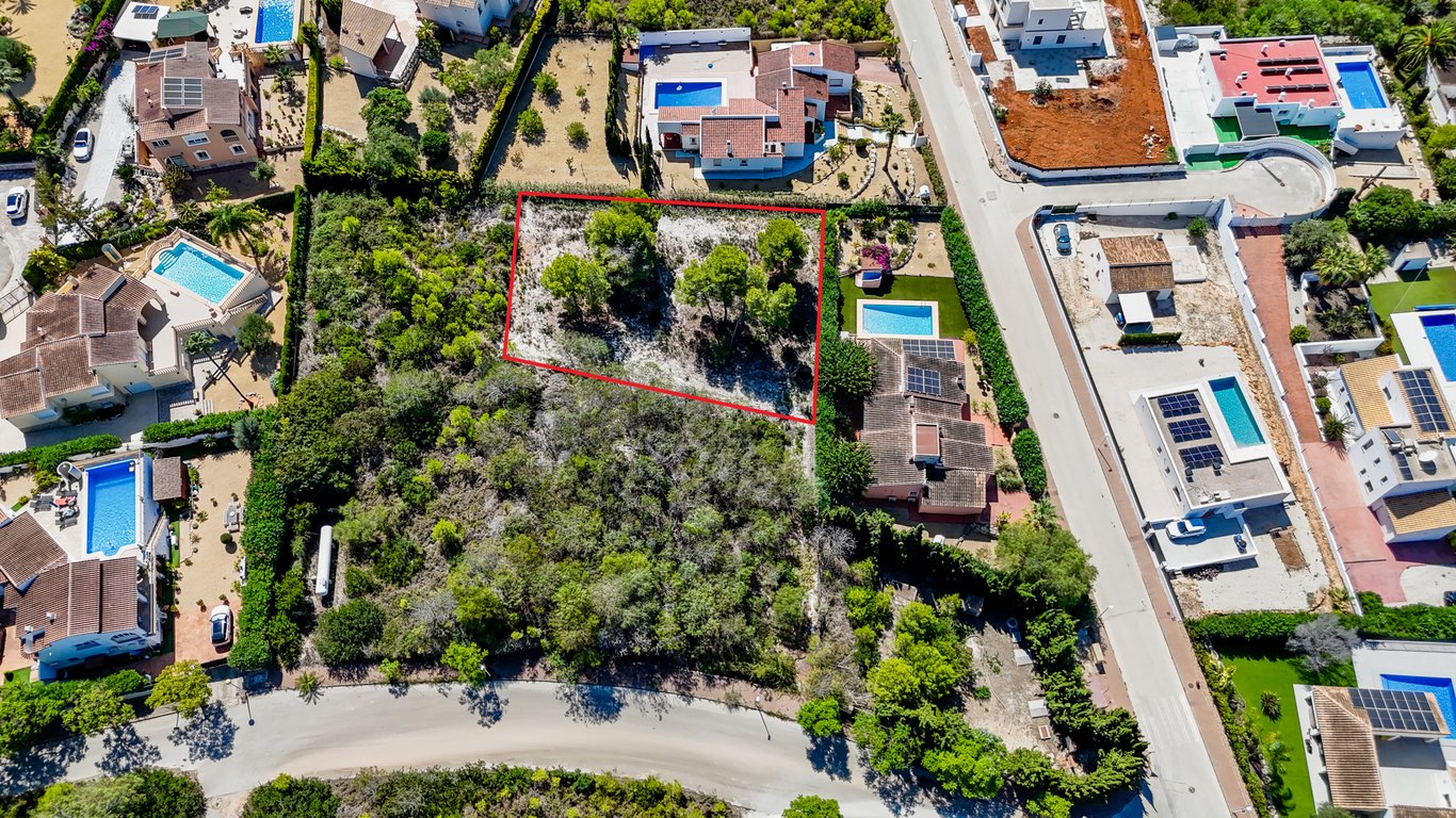 Vista aérea de la parcela urbana edificable delimitada en rojo, situada junto a la villa principal con piscina y paneles solares en una zona residencial consolidada.