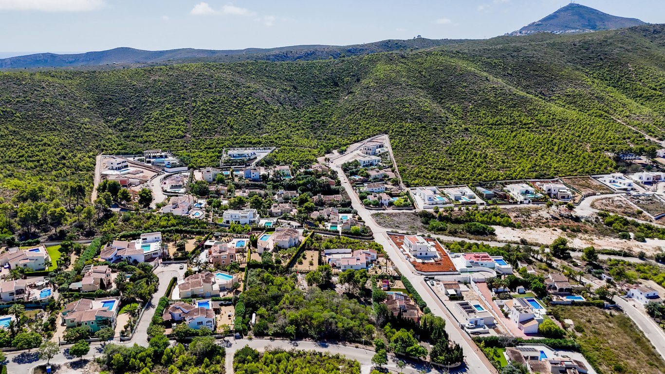 Vista aérea de la urbanización residencial en Jávea, destacando la integración de las villas con piscina en el entorno natural de colinas verdes.