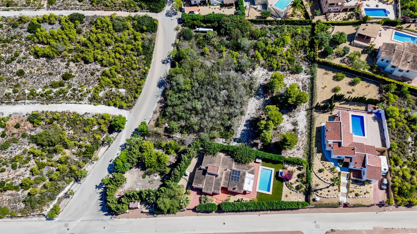 Vista aérea de la villa con paneles solares y piscina, junto a la extensa parcela urbana colindante con vegetación natural en Jávea.