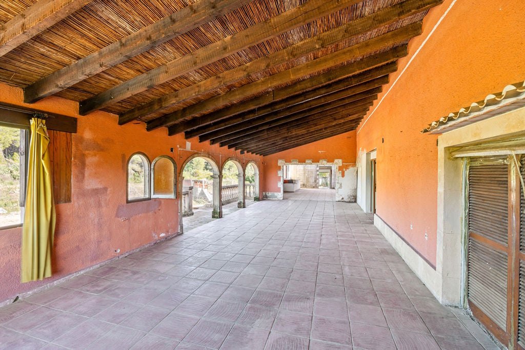 Amplia naya con techos de vigas de madera y cañizo, paredes en tono terracota y arcos de piedra que dan paso a los exteriores de la propiedad.