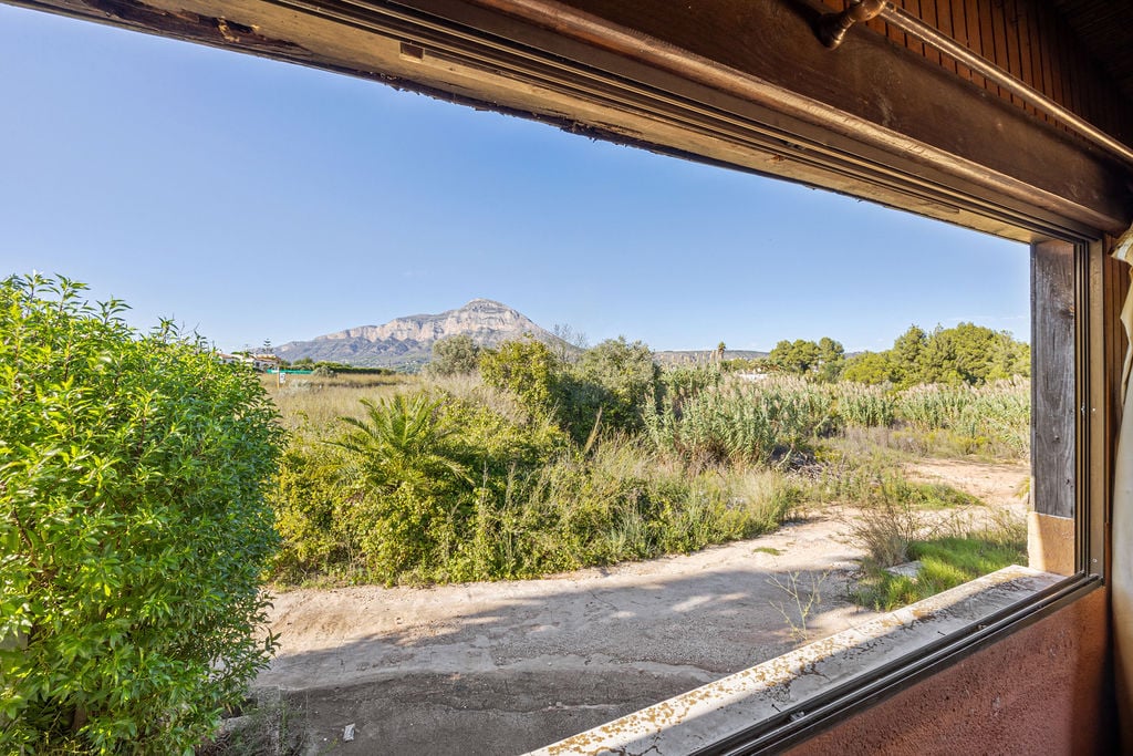 Vista panorámica del macizo del Montgó desde un ventanal con marco de madera. El entorno exterior destaca por su vegetación mediterránea autóctona y cielos despejados.