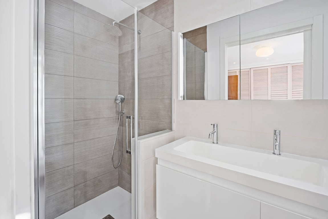 Baño moderno con ducha de obra en gres gris texturizado, mampara de vidrio y mueble de lavabo suspendido blanco con grifería de diseño contemporáneo.