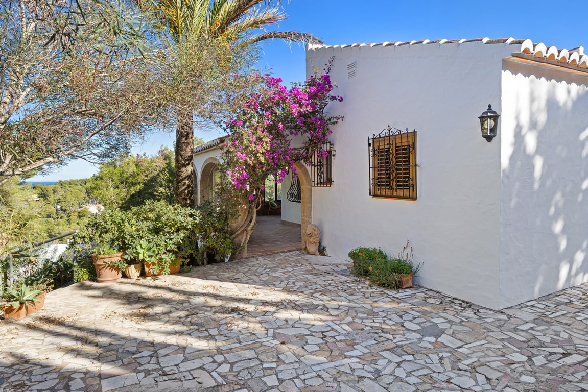 Fachada blanca tradicional con arcos de piedra Tosca, buganvilla en flor y terraza de piedra irregular con vistas al entorno natural de Jávea.