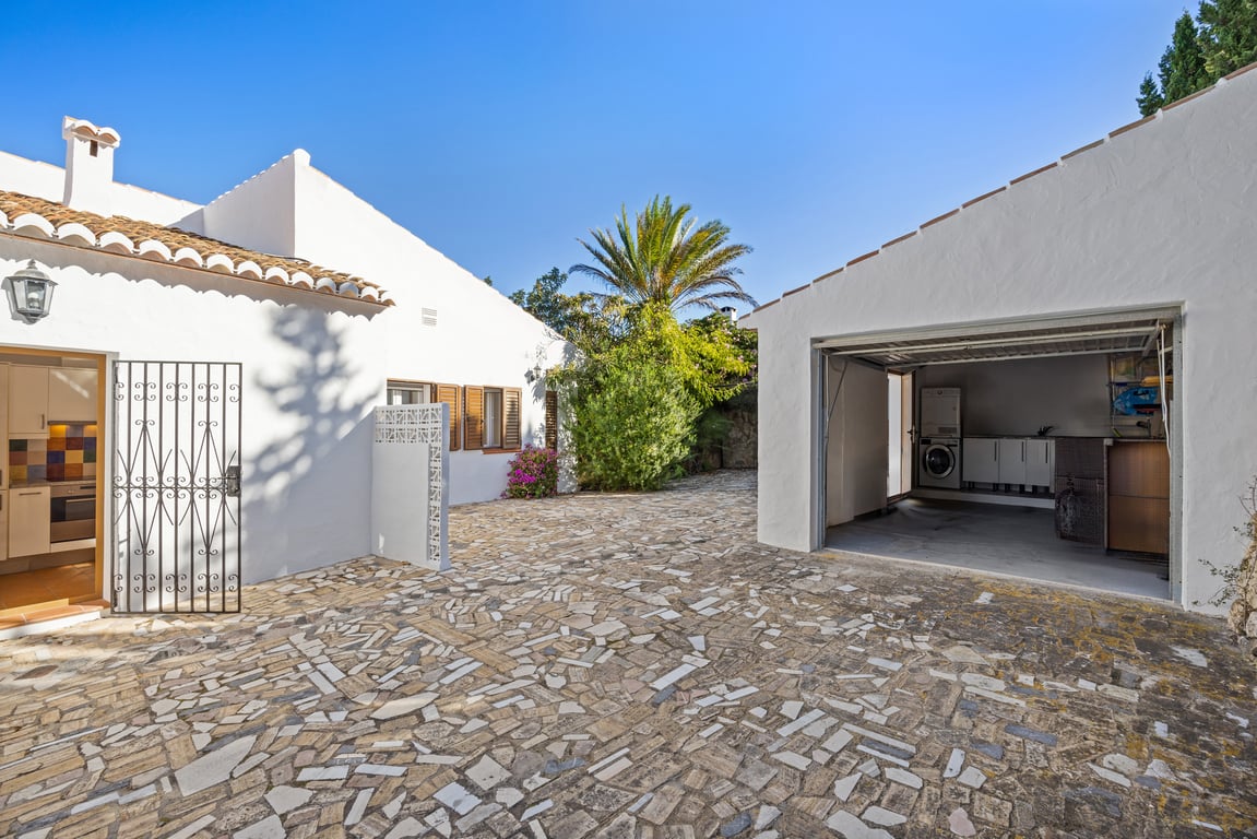 Patio exterior pavimentado en piedra con acceso a la cocina y un garaje independiente que integra una zona de lavandería equipada.
