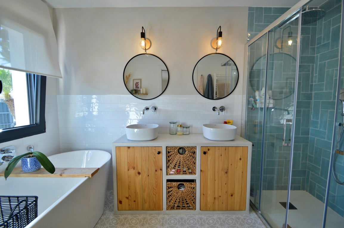 Baño moderno con lavabo doble, mueble de madera y mimbre, bañera exenta y una ducha de obra revestida con azulejos turquesas y mampara de cristal.
