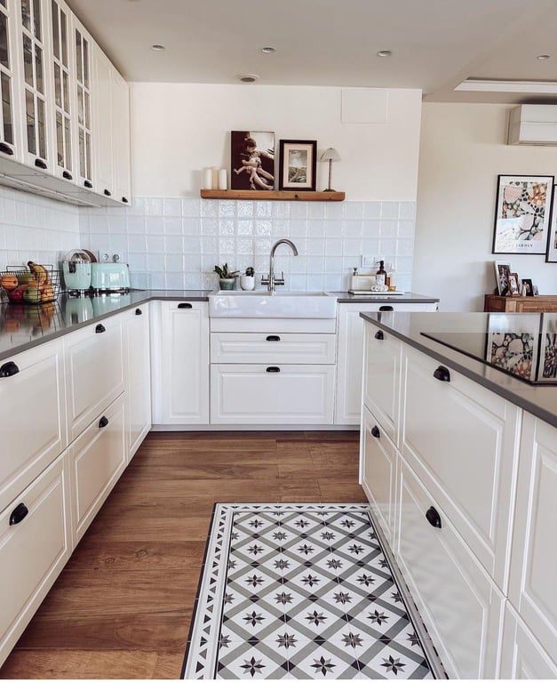 Cocina moderna de estilo rústico con armarios blancos, encimera oscura y fregadero de cerámica. Destaca el suelo de madera con un mosaico central de baldosas hidráulicas decorativas.