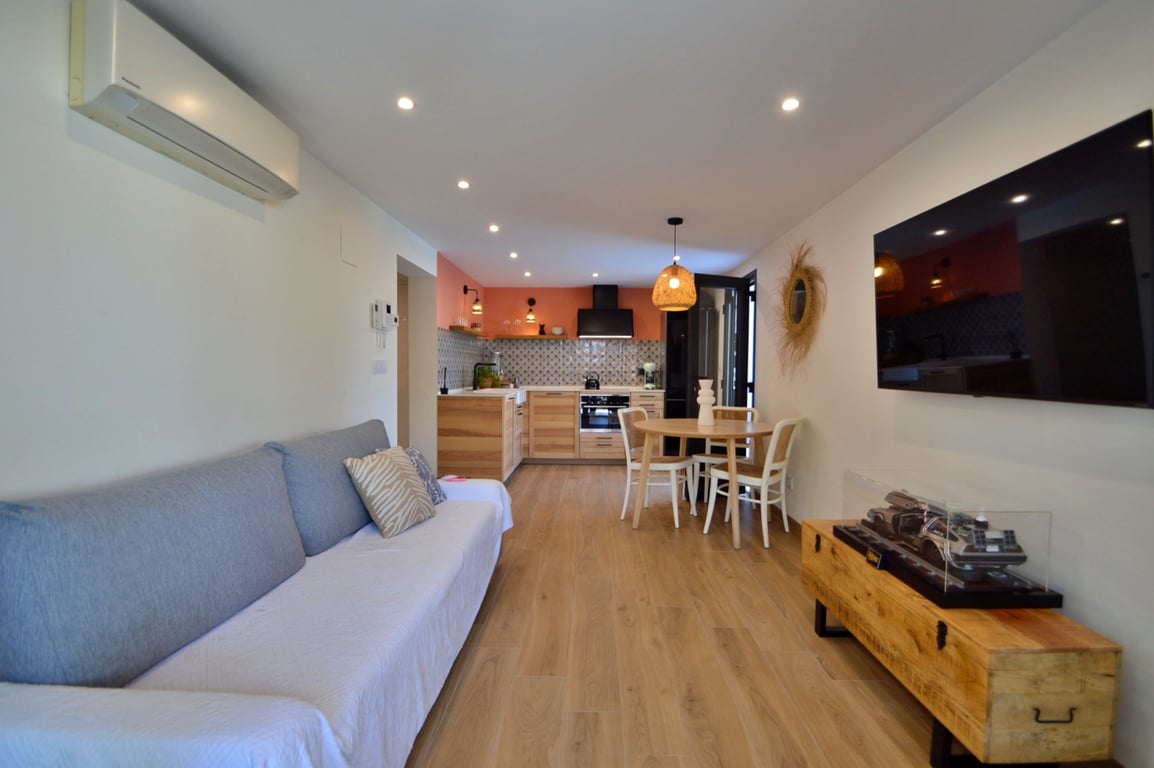 Salón comedor de concepto abierto con cocina integrada, suelos de madera, aire acondicionado y zona de estar con televisión de pantalla plana.