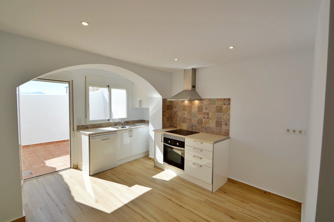 Cocina moderna renovada con armarios blancos, salpicadero de azulejos decorativos y acceso directo a un patio privado soleado.