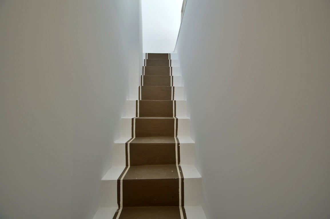Escalera interior de diseño minimalista con peldaños en tono marrón y bordes blancos, iluminada por luz natural cenital.