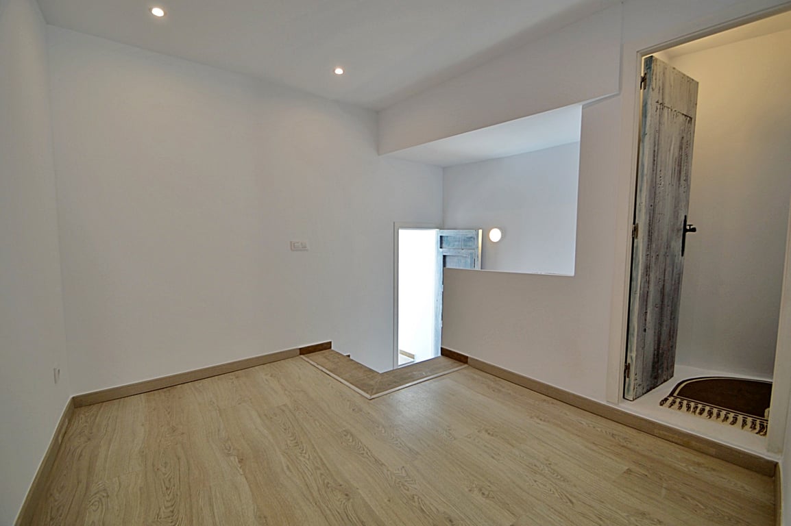 Estancia intermedia versátil con suelos de tarima clara, iluminación LED empotrada y una puerta de madera de estilo rústico restaurada.