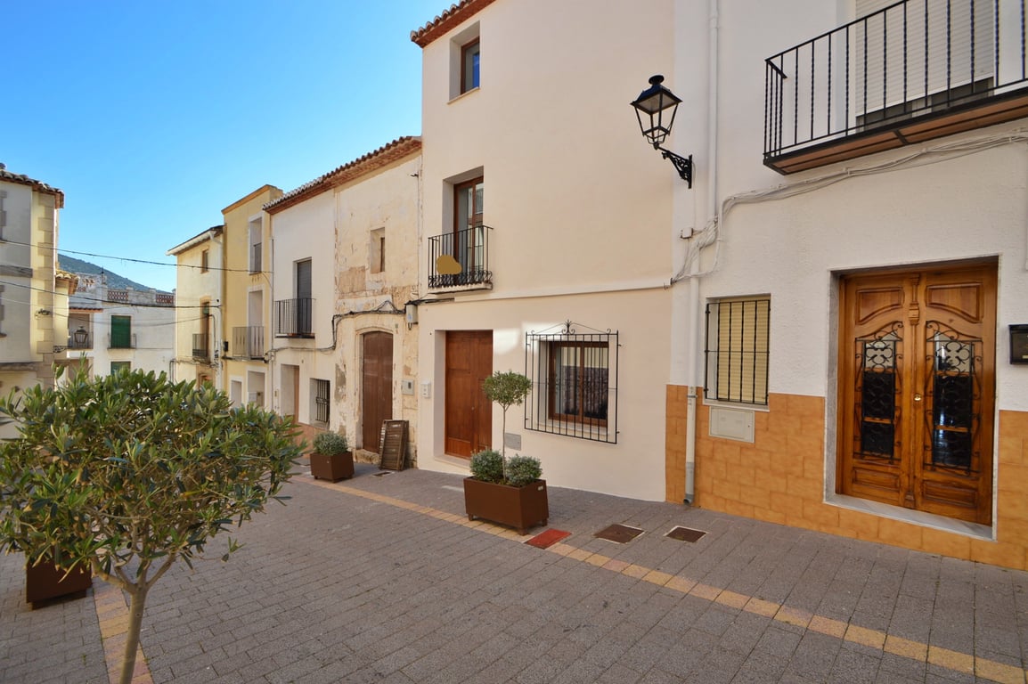 Fachada exterior renovada en calle peatonal con puerta de madera, rejas de hierro forjado y maceteros decorativos bajo un cielo despejado.