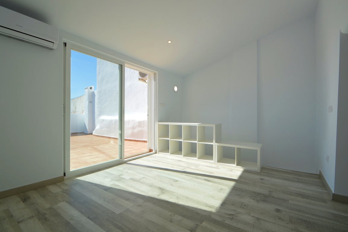Habitación luminosa con suelos de tarima clara, aire acondicionado y acceso directo a la terraza mediante un gran ventanal corredero de cristal.