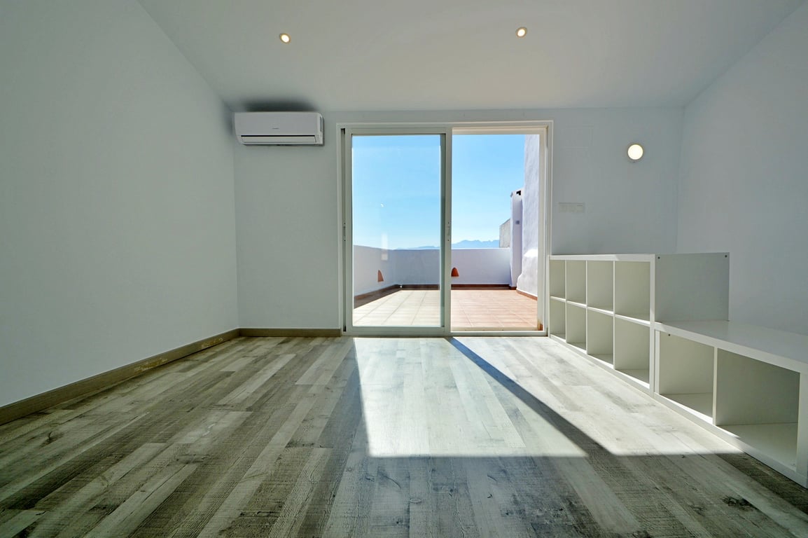 Habitación luminosa con suelos laminados, aire acondicionado y acceso directo a la terraza superior mediante puertas correderas de cristal.