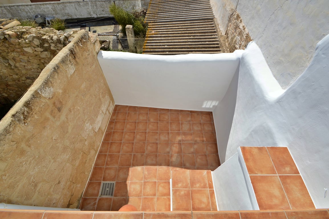 Terraza privada con suelos de baldosas de terracota, muros encalados en blanco y una pared lateral de piedra original que aporta carácter rústico.