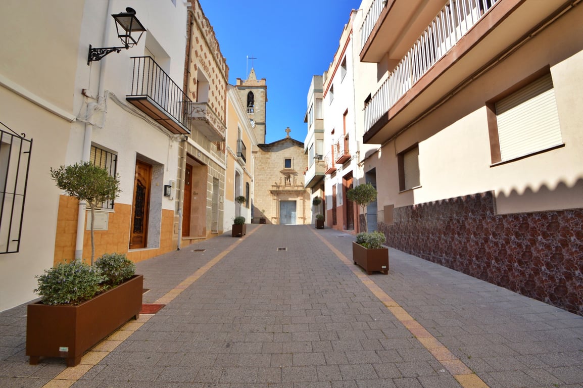 Vista exterior de una calle peatonal empedrada que conduce a una iglesia histórica, rodeada de fachadas tradicionales con balcones de forja.