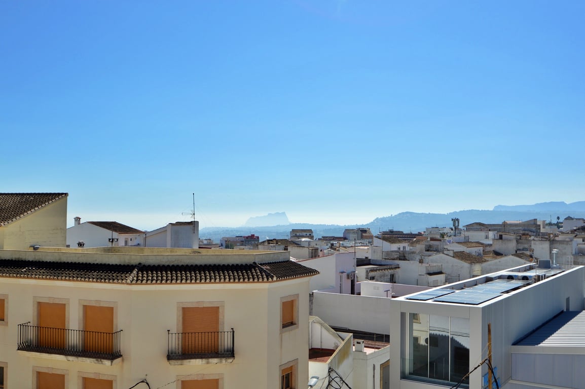 Vistas panorámicas desde la terraza hacia los tejados del pueblo, con la silueta de las montañas y el mar Mediterráneo en el horizonte bajo un cielo despejado.