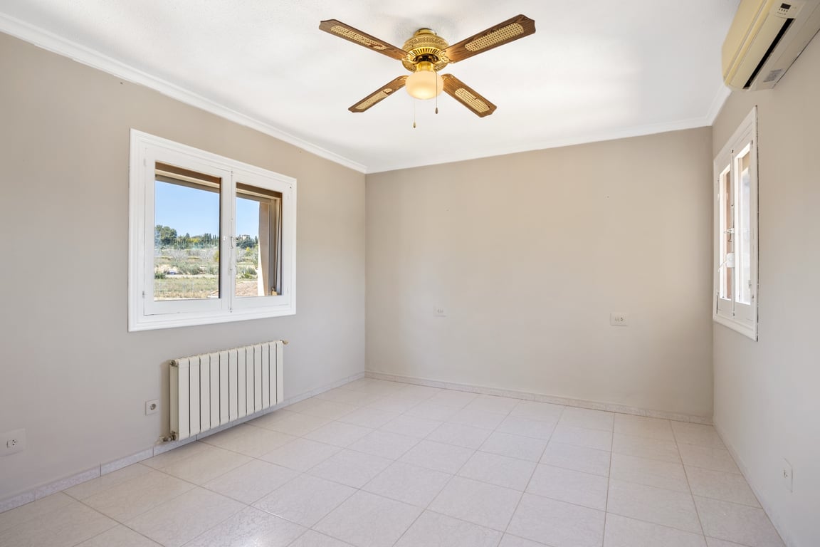 Dormitorio luminoso con suelos de gres, ventilador de techo, aire acondicionado y radiador. Las ventanas ofrecen vistas despejadas al entorno natural de Jávea.