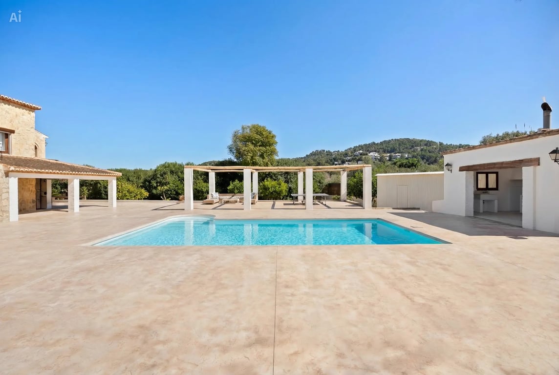 Piscina de 5x10 metros rodeada de una amplia terraza pavimentada, con pérgola de madera, cocina exterior y vistas despejadas a las montañas de Jávea.