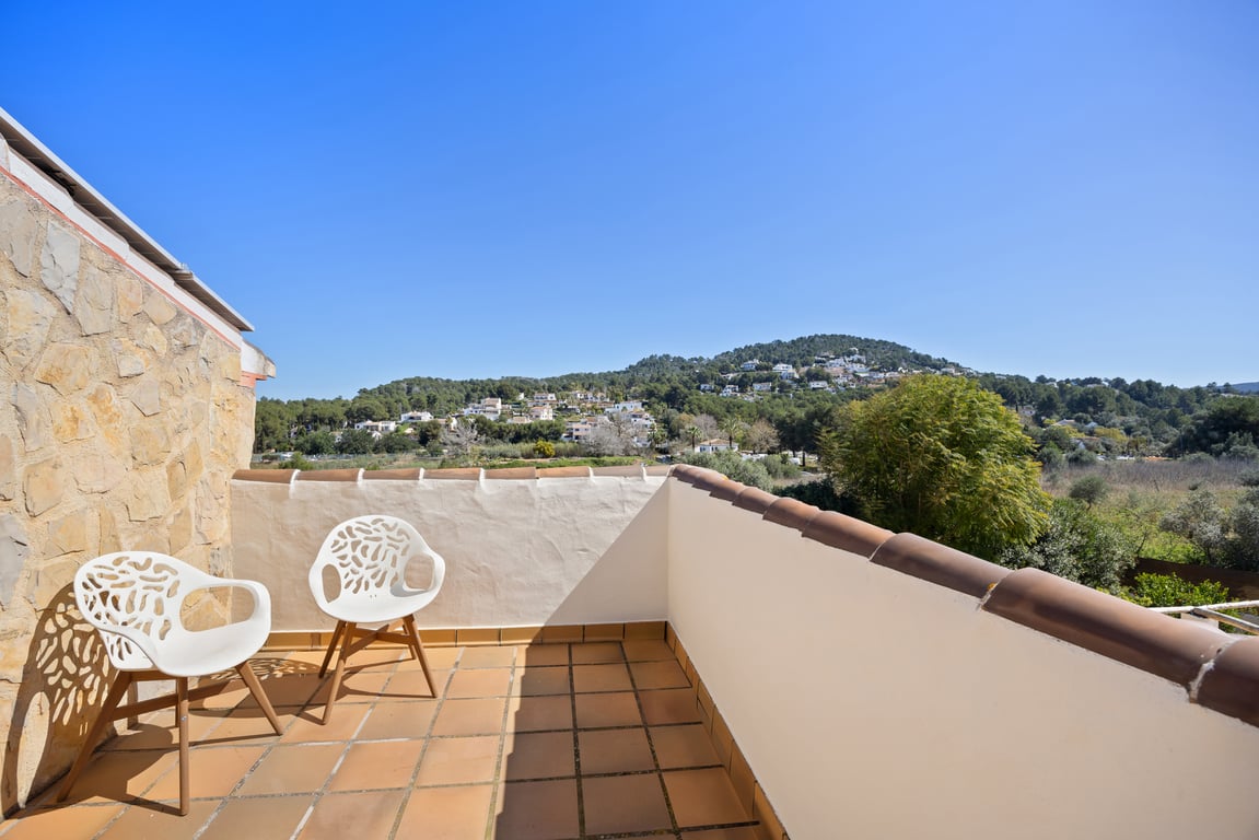 Terraza privada en la planta superior con suelo de barro, sillas de diseño y vistas despejadas hacia las colinas circundantes de Jávea.