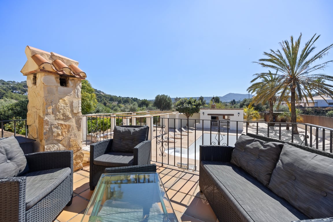 Terraza superior con mobiliario de exterior en ratán, suelos de terracota y vistas despejadas a la zona de piscina, cocina de verano y las montañas circundantes.