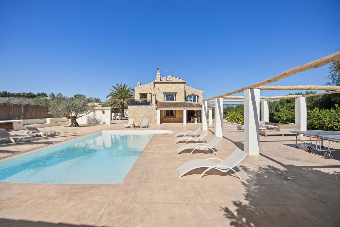 Vista exterior de la villa de piedra con piscina de 5x10m, amplia terraza de solárium, zona de pérgola y mesa de ping-pong en una parcela orientada al sur.